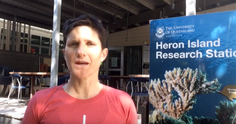 Dr Karen Joyce standing next to the Heron Island Research Station poster