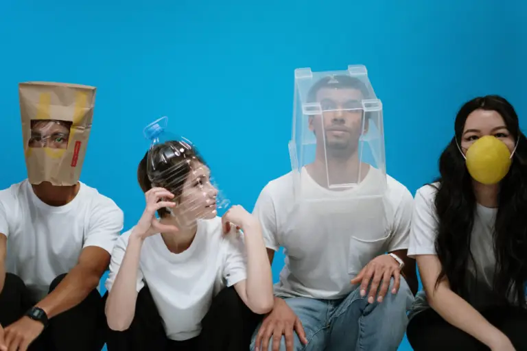 four young adults try to shield themselves with a plastic water container, storage box, mask, and paper bag