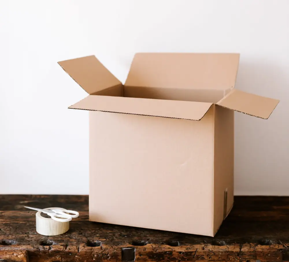 cardboard box, packaging tape, and scissors sitting on a wooden table