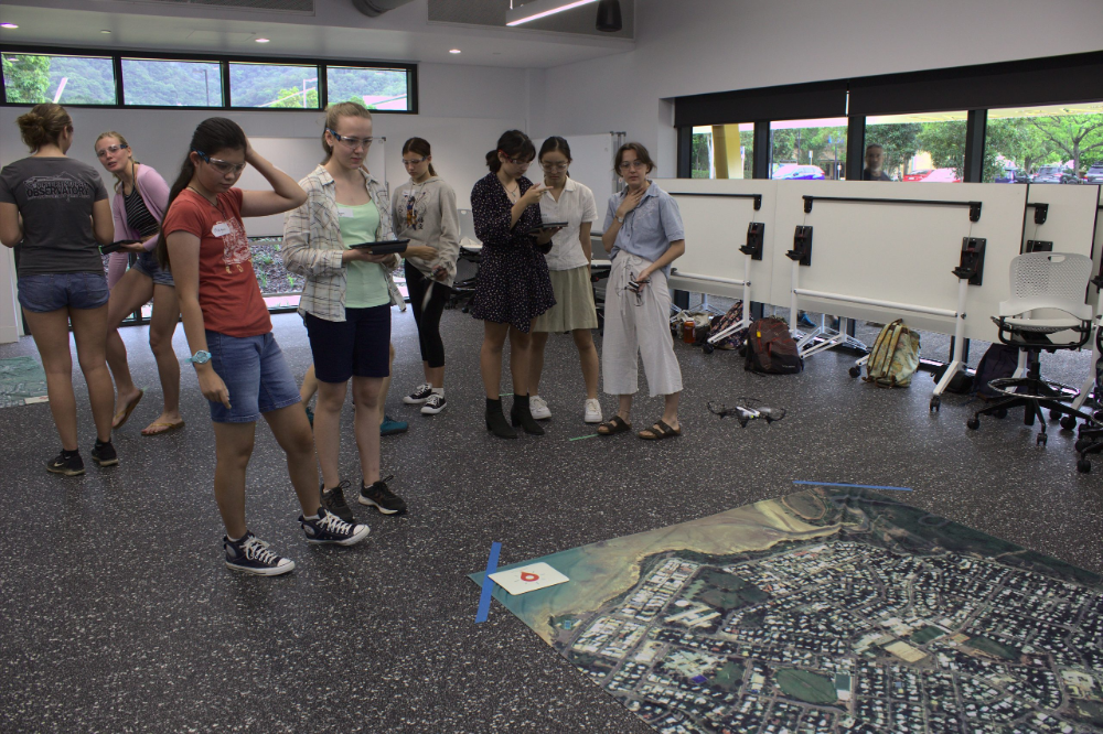 a group of female students looking at the image mat laid out flat on the floor as part of their drone lessons