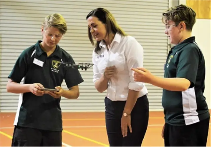 two young boys flying a drone under the supervision of their female teacher