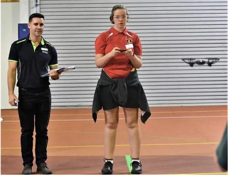 David Capilla standing next to his student who is flying a drone inside the school gymnasium