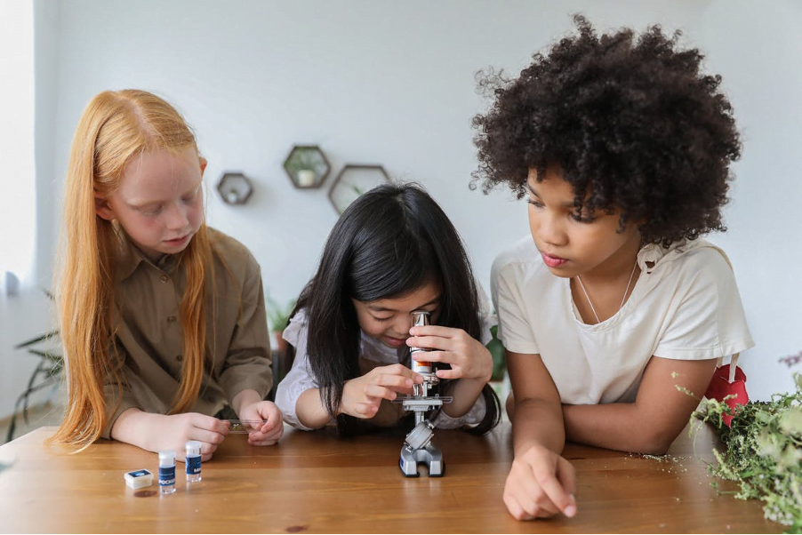 young girls gathering around a microscope