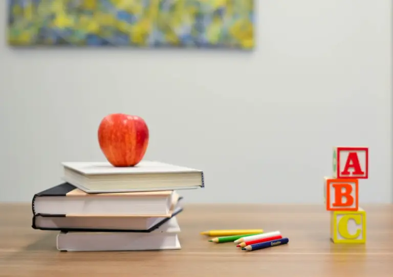 red apple and notebooks, letter blocks, and colour pencils on a table