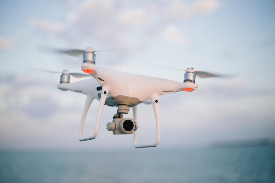 White drone with a camera flying over a body of water