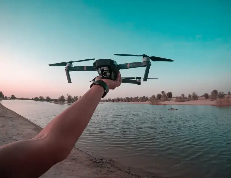 a person holding a drone up over a body of water