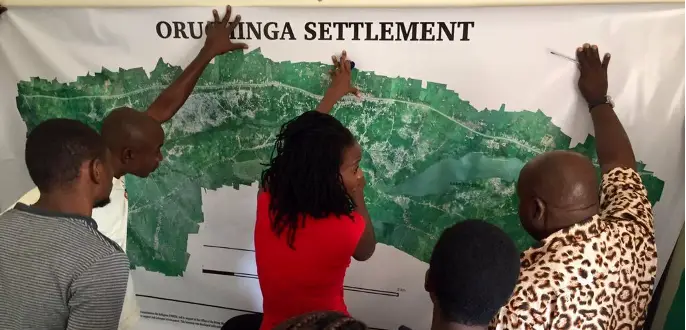 Remote sensing in agriculture men helping a woman hold up a settlement map against a wall