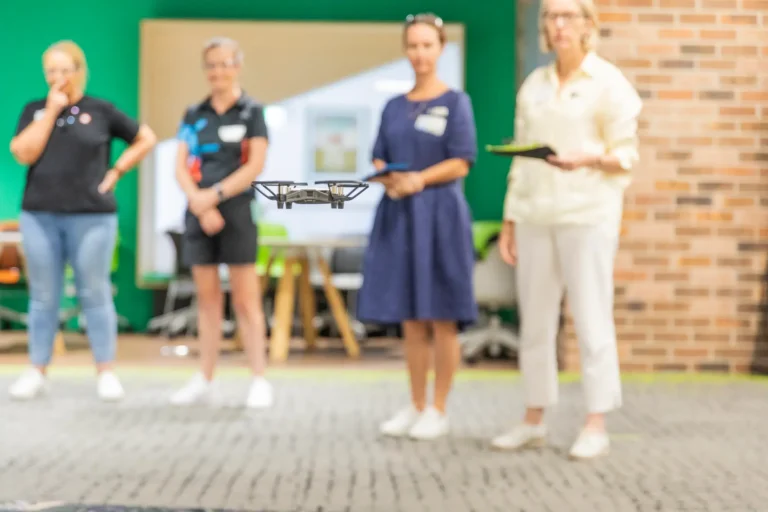 Teachers watching a flying drone indoors.