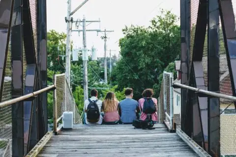 Four friends sitting on pedestrian bridge with backpacks