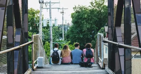 Four friends sitting on pedestrian bridge with backpacks