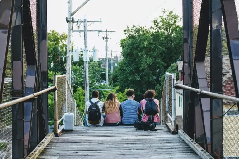 Four friends sitting on pedestrian bridge with backpacks
