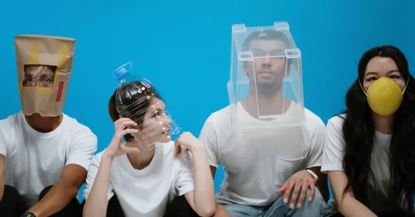 four young adults try to shield themselves with a plastic water container, storage box, mask, and paper bag