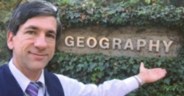 Renowned geographer Dr Joseph Kerski strikes a pose beside a Geography letter logo