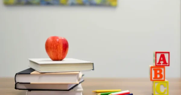 red apple and notebooks, letter blocks, and colour pencils on a table